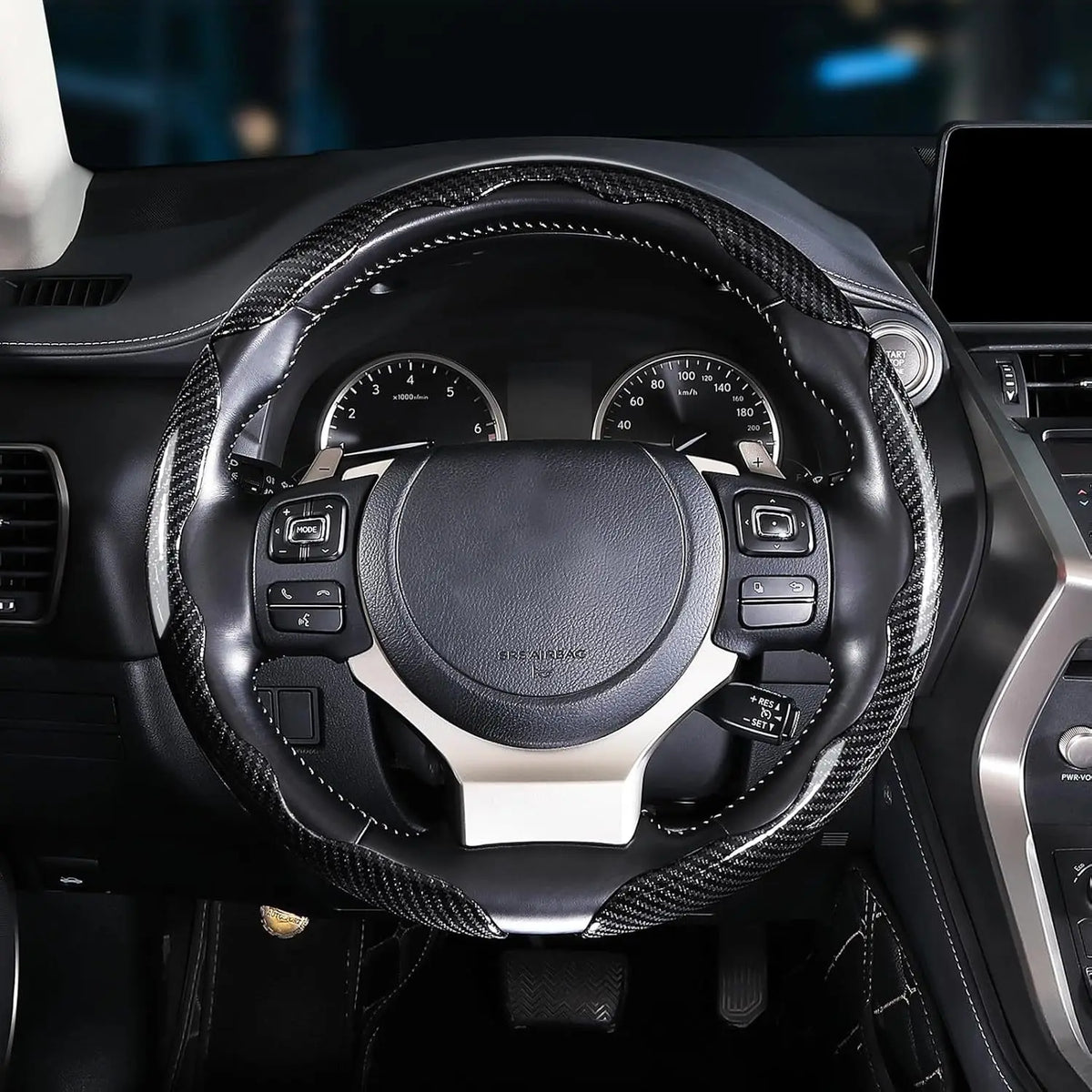 Close-up view of a black steering wheel with carbon fiber accents and controls inside a car interior.