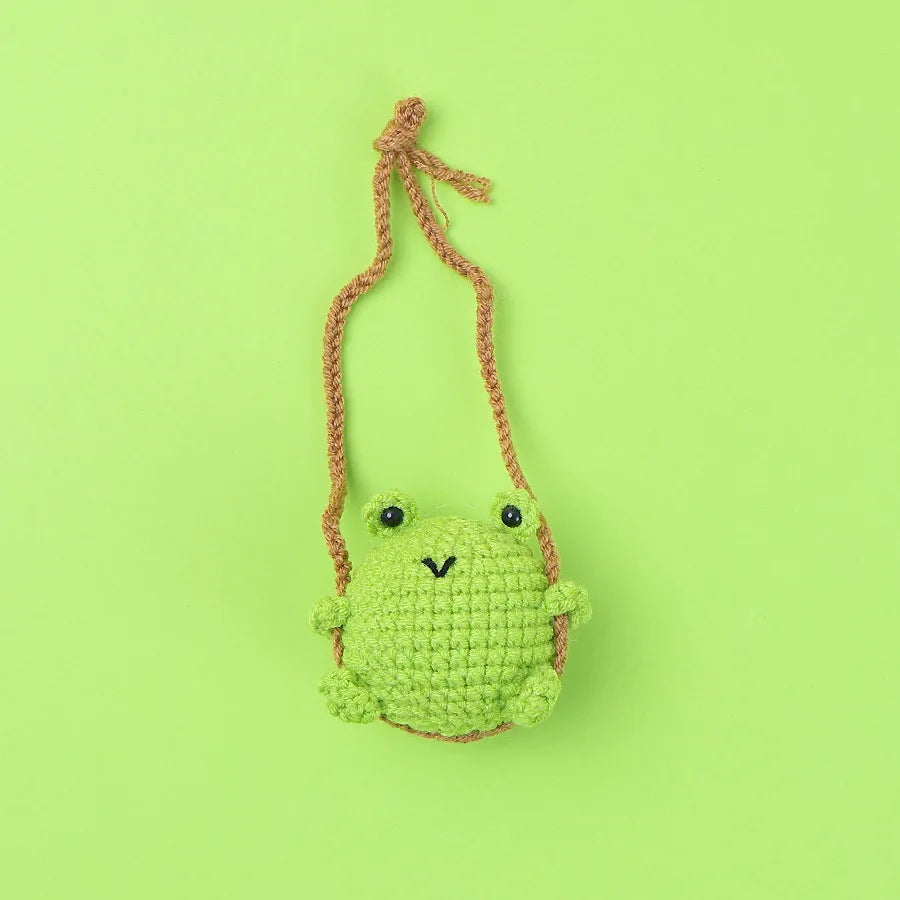 A handmade strawberry crochet hanging charm featuring a green frog with a pink string.