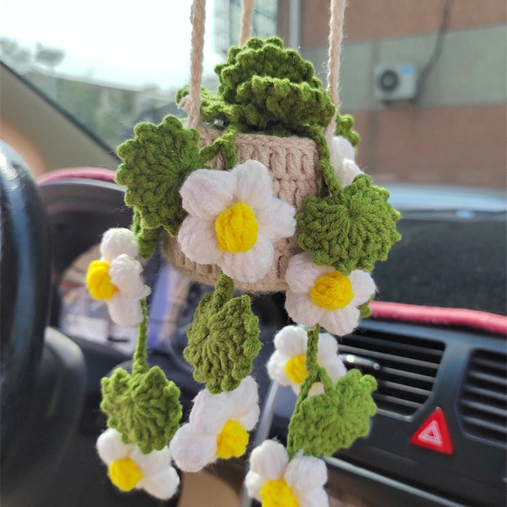 A hanging crochet strawberry decor featuring white and yellow flowers in green mossy leaves, displayed inside a car.