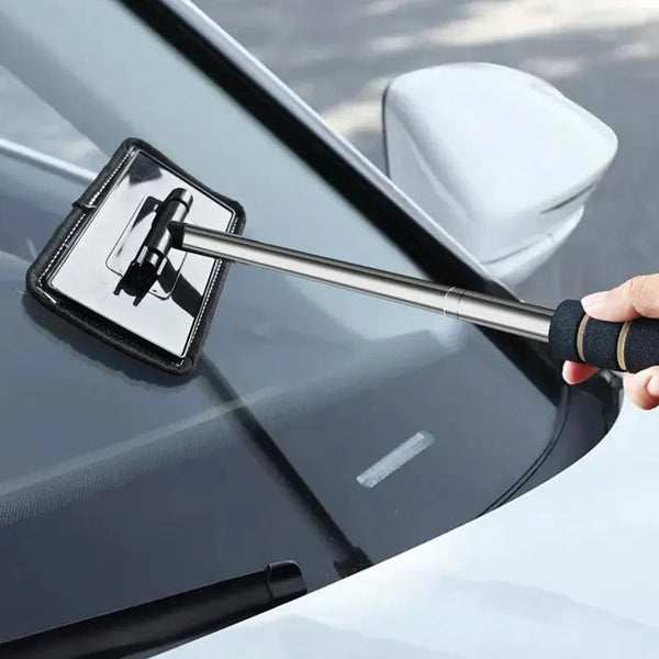 A hand uses a telescopic windshield cleaning brush to wipe the glass of a car.