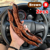 Two brown leather steering wheel booster covers are held in a hand, displayed on a car steering wheel.