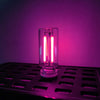 A clear glass cylindrical LED night light with bright pink illumination resting on a black tray.