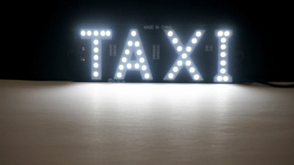 A close-up of an LED taxi sign displaying the word TAXI, illuminated against a dark background.