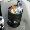 A black waterproof collapsible car bin bag is hanging on a car seat, filled with various items including a bottle and some fo