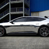 A silver car with a glossy chrome vinyl wrap is parked outdoors in front of an industrial building.
