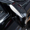A close-up of a black car's rearview mirror with a rhinestone rain shield visor attached.