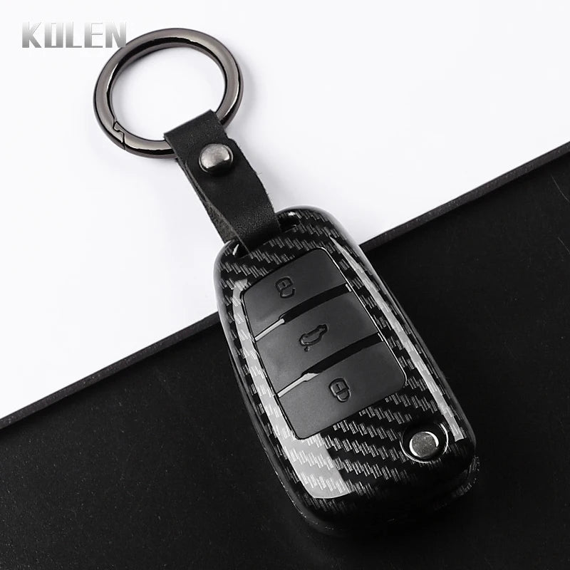 A black carbon fiber car key case cover with a metal keyring is shown on a dark surface.