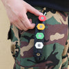 A hand holds a black high-pressure washer gun with various colored foam cannon nozzles against a camouflage fabric.