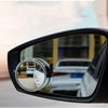 A close-up view of a black car mirror with a dual lens blind spot mirror attached.