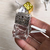 A clear glass car air freshener bottle with a silver mesh top and a white dispenser is held in a hand.