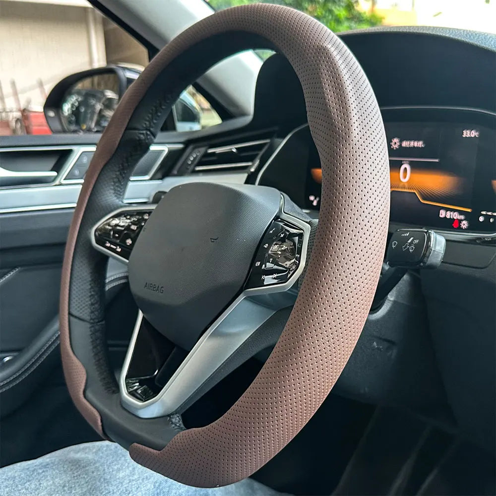 Nahaufnahme einer tanfarbenen Lederlenkradabdeckung im Autointerieur, zeigt Airbag und Bedienelemente.