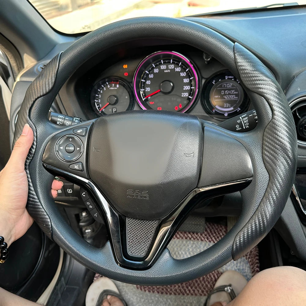 A close-up view of a black steering wheel with controls and a leather-like grip, inside a car cabin.