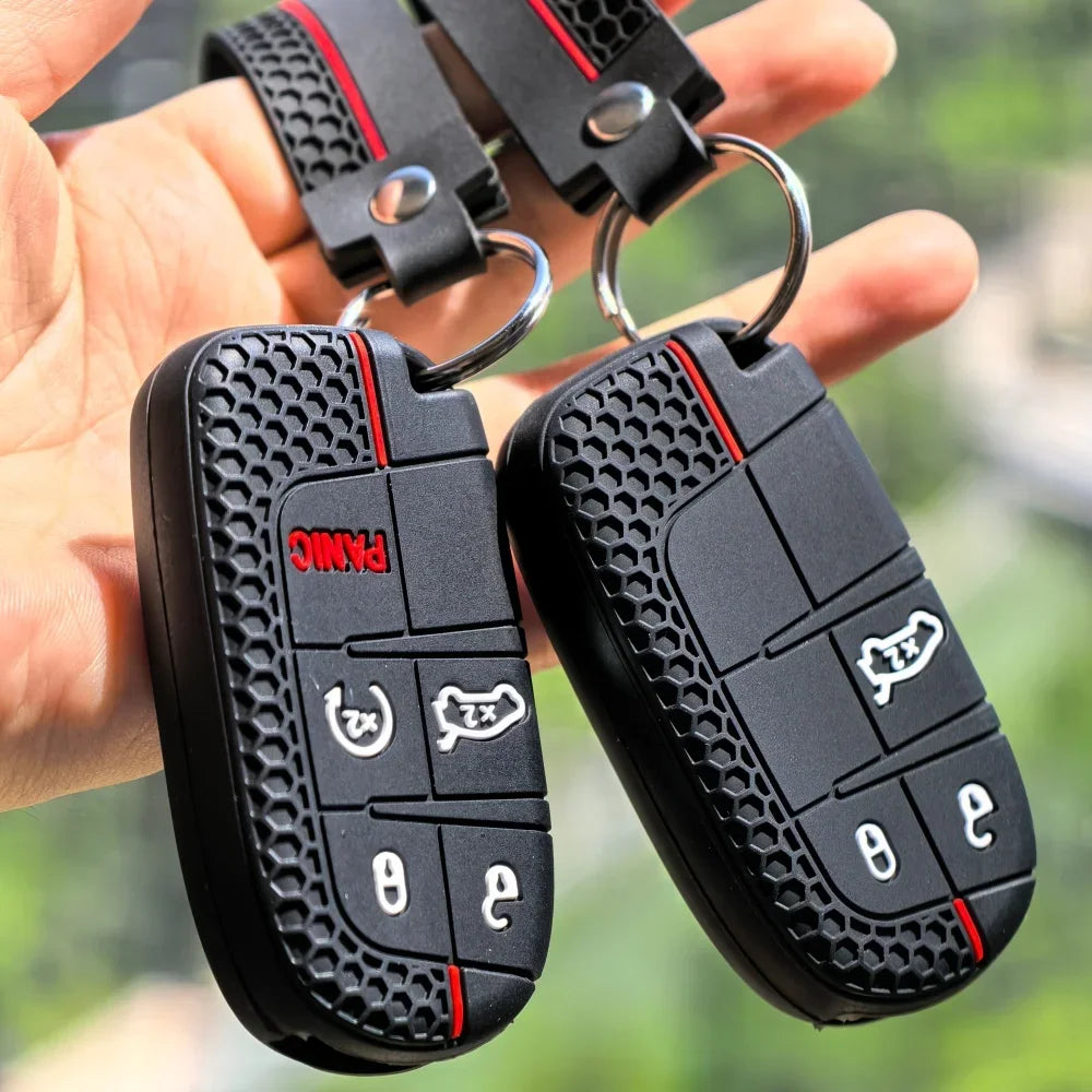 A hand holds a black silicone car key cover for Jeep, Dodge, and Chrysler models with attached keyring loops.