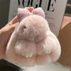 A pink plush bunny keychain with soft fur and a gold ring is being held against a background featuring a Vogue magazine.