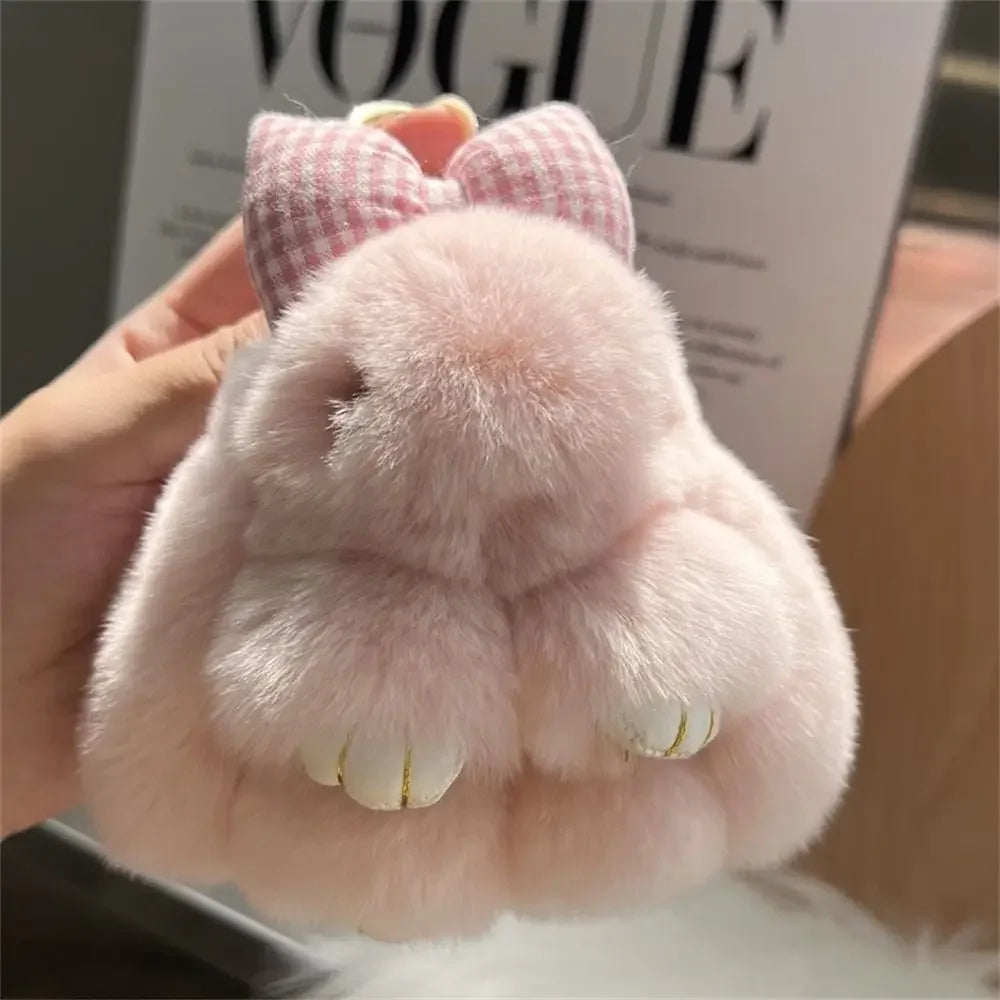A pink plush bunny keychain with soft fur and a gold ring is being held against a background featuring a Vogue magazine.