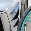 Close-up of a white car bumper with black spoiler fins and a tire visible.