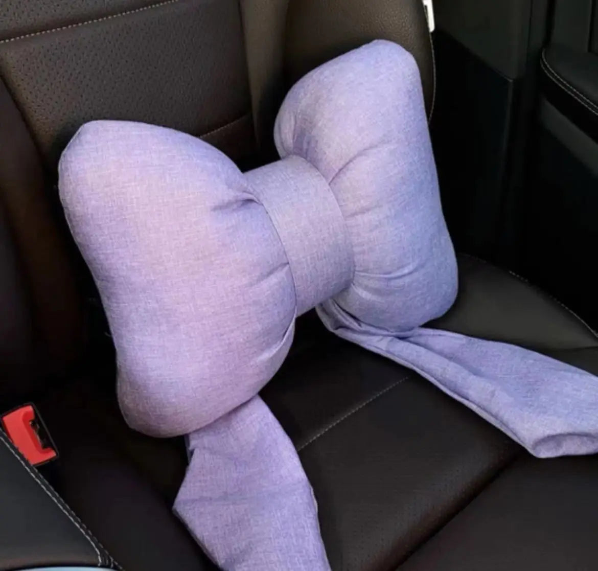 Un oreiller de cou accent butterfly en tissu violet clair posé sur un dossier de voiture sombre.