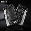A black carbon fiber button cover for a car key, featuring embossed symbols and a silver stud.