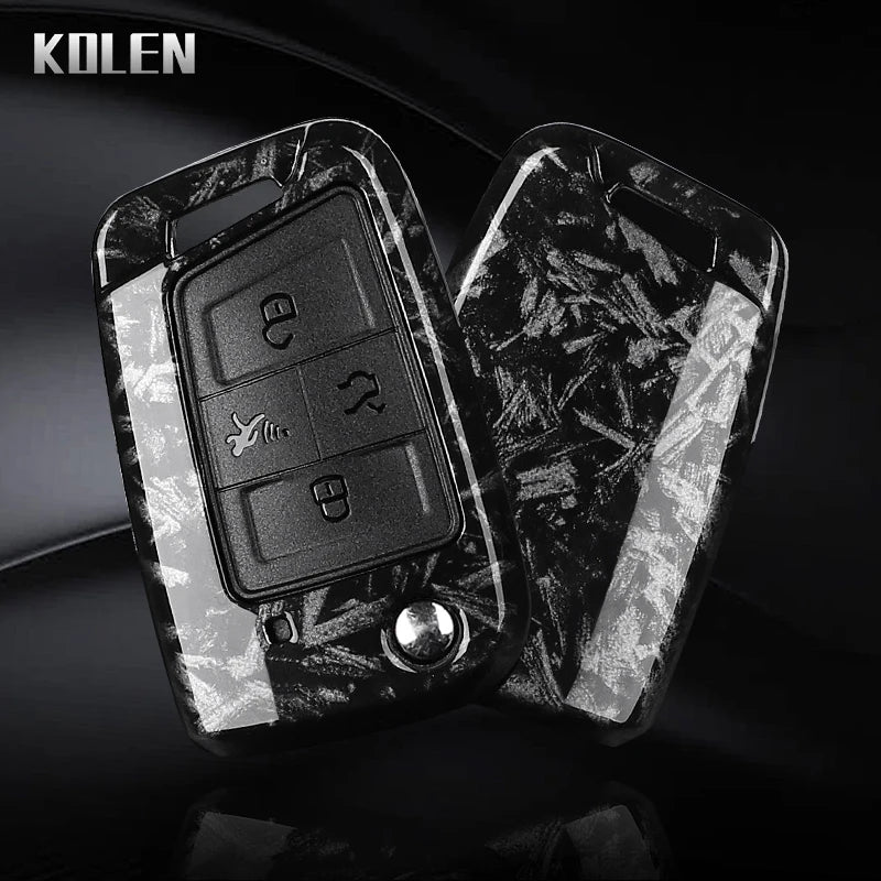 A black carbon fiber button cover for a car key, featuring embossed symbols and a silver stud.