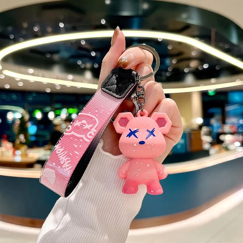 Une main tient un jouet en peluche rose en forme d'ours avec des marques de larmes attachées à une housse de boîte à clés en 