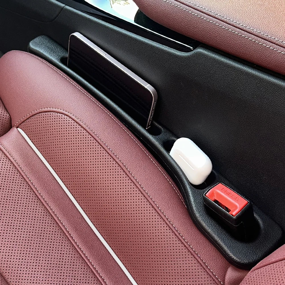 A close-up view of a car seat gap filler strip with a black and white design resting in a pink leather interior.