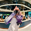 Une main tient un porte-clés de peluche violet attaché à une housse de clé en cuir dans un cadre moderne.