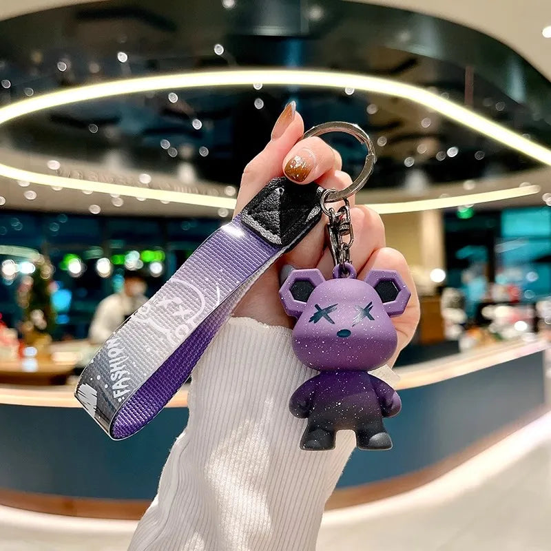 Une main tient un porte-clés de peluche violet attaché à une housse de clé en cuir dans un cadre moderne.