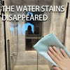 A hand is holding a light blue reusable glass cleaning cloth against a glass shower door.