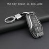 A black carbon fiber style key fob cover with a metal chain is shown resting on a dark surface.