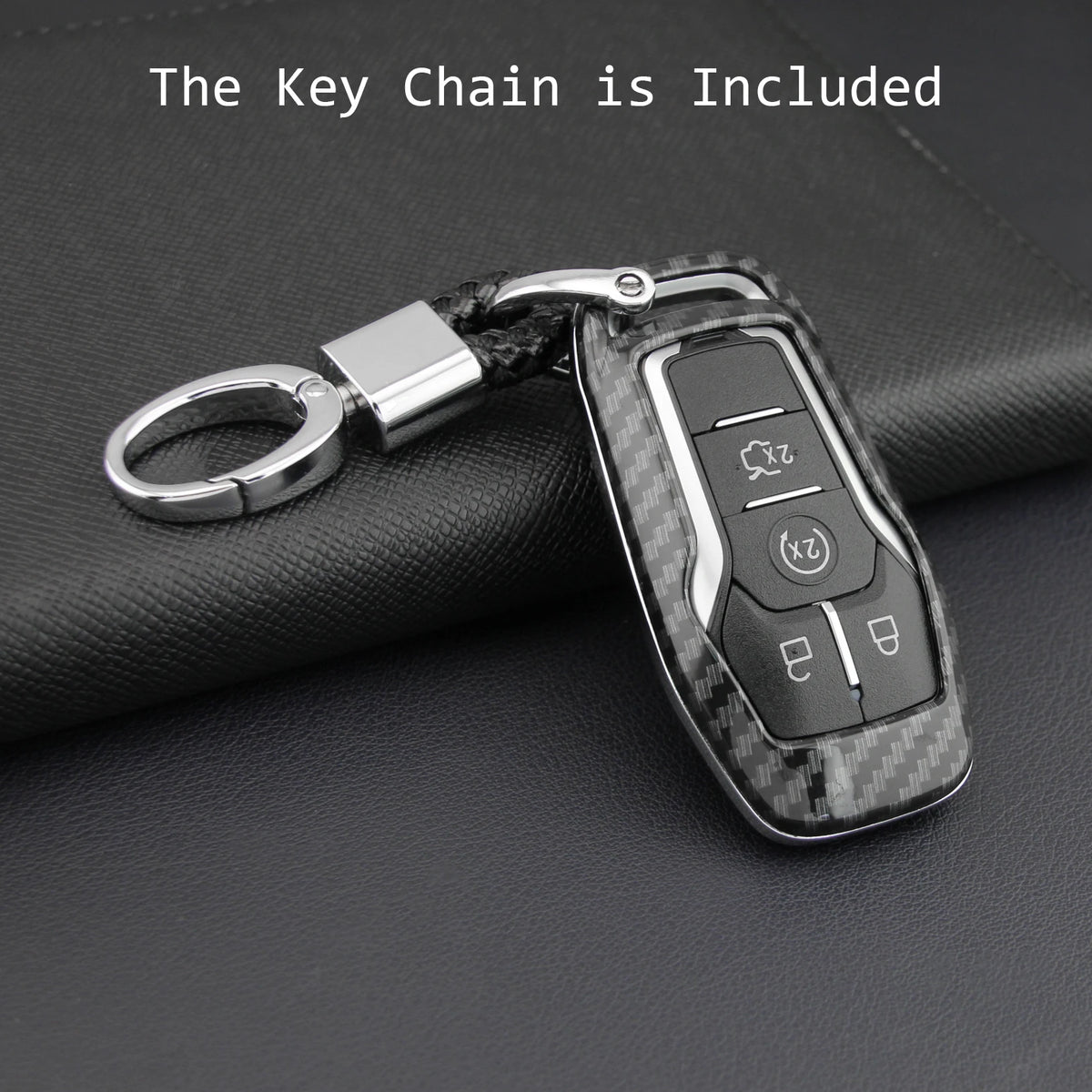A black carbon fiber style key fob cover with a metal chain is shown resting on a dark surface.
