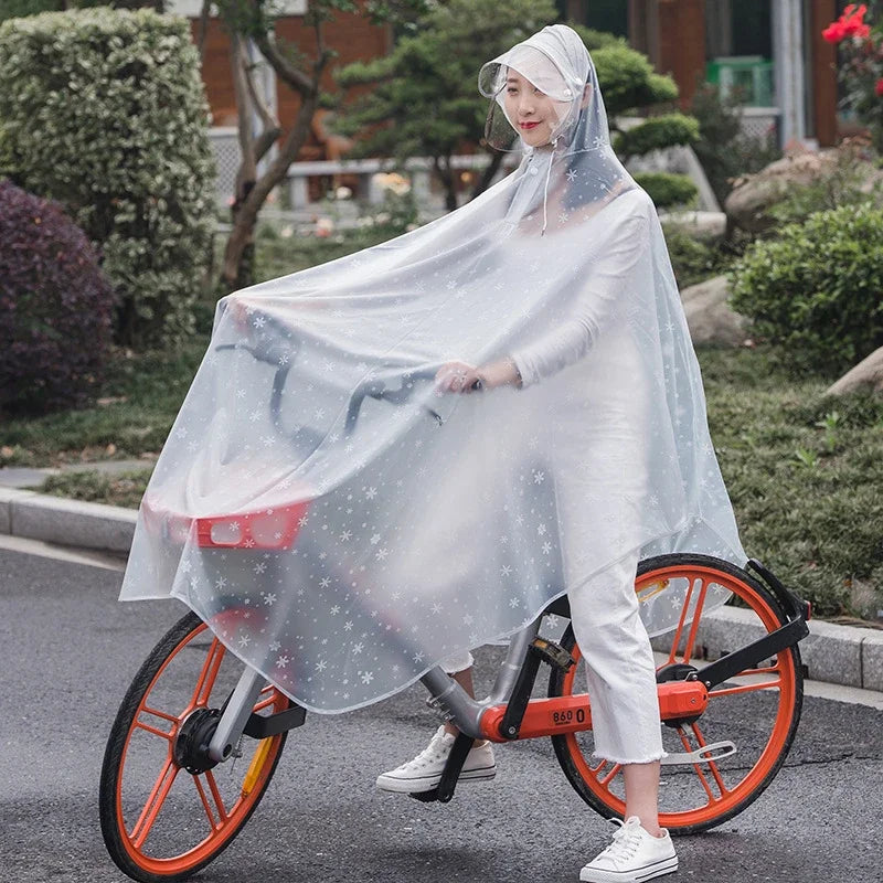 A woman wearing a transparent windproof motorcycle rain poncho rides an orange bicycle on a paved road.