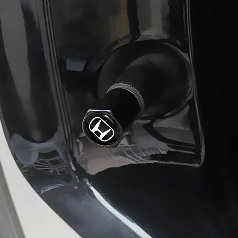 Close-up of a black tire valve cap with a silver logo on a dark automotive surface.