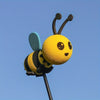 A yellow bee antenna decoration with black stripes and blue wings against a clear blue sky.