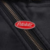 A close-up of a black leather surface showing a red Peterbilt oval enamel lapel pin on a stitched seam.
