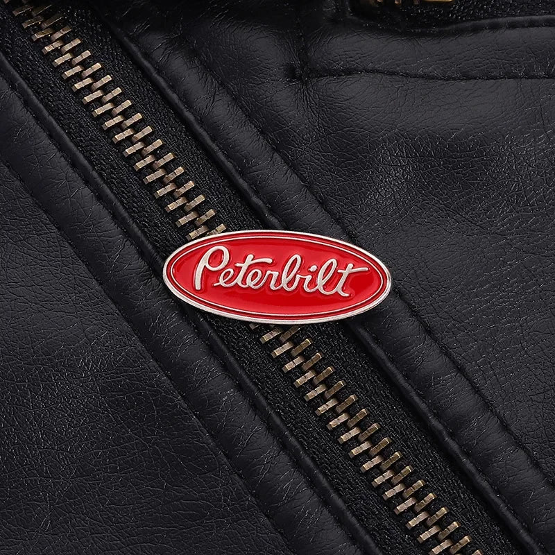 A close-up of a black leather surface showing a red Peterbilt oval enamel lapel pin on a stitched seam.