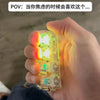 A hand holds a clear illuminated mechanical keyboard keychain, showing bright green and yellow light.