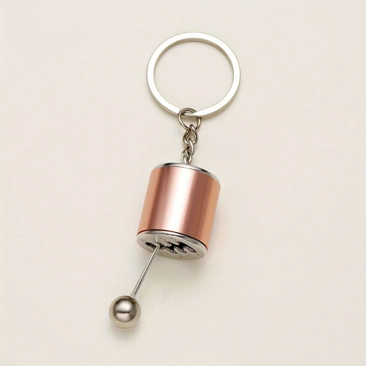 A rose gold metal keychain featuring a cylindrical charm and a circular keyring.