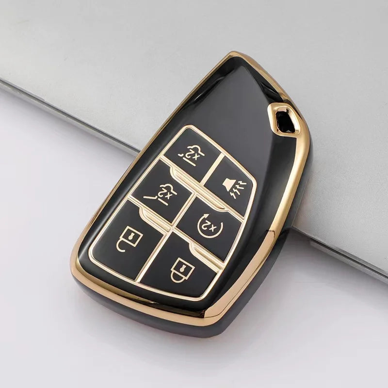 A black multi-function car key cover with gold accents shown on a gray surface.