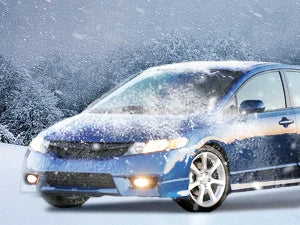 A blue Honda Civic sedan is shown with fog lights illuminated, covered in falling snow.