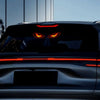 Close-up of a dark car with bright red demonic eye lights illuminated on the rear window and trunk.