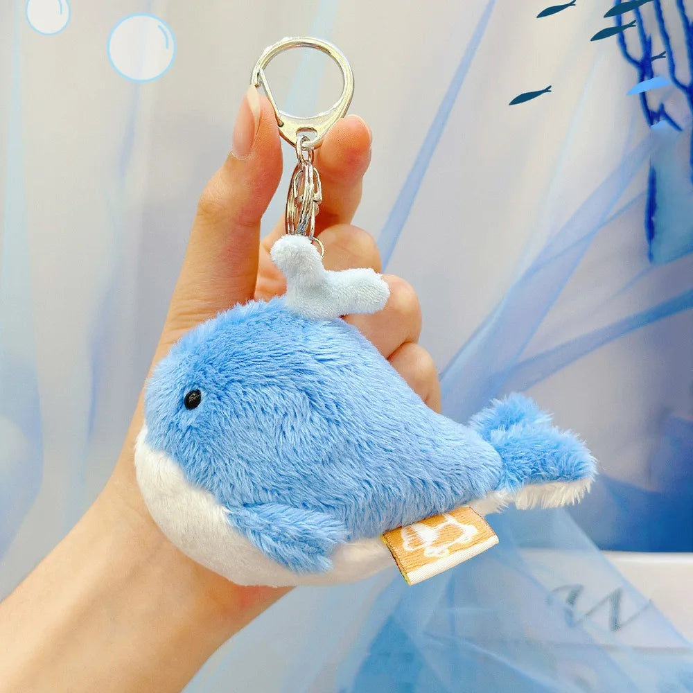 A hand holds a blue and white plush bunny keychain with soft fur attached to a gold ring.