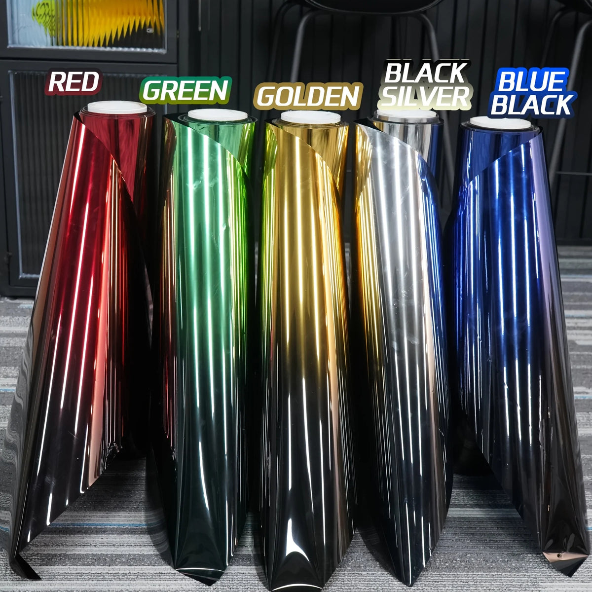 A display of color changing solar window tint film rolls in red, green, golden, black, silver, and blue.