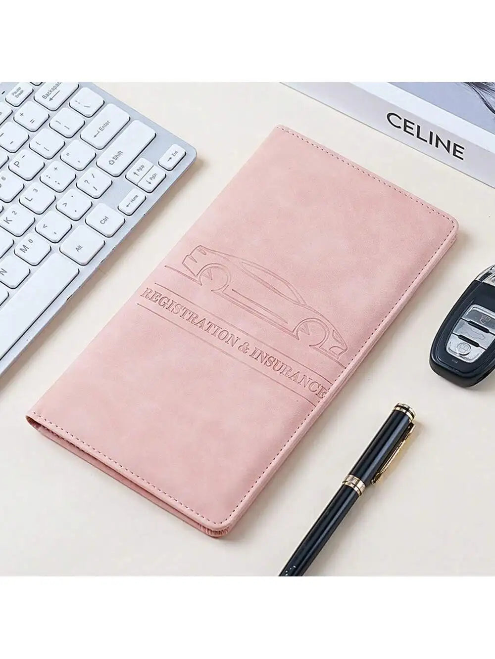 Pinkes Lederdokumentenhalter mit Auto-Silhouette, neben einer weißen Tastatur und einem schwarzen Stift.
