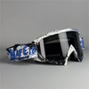 Un par de gafas de motocicleta negras con detalles gráficos blancos y azules sobre una superficie gris.