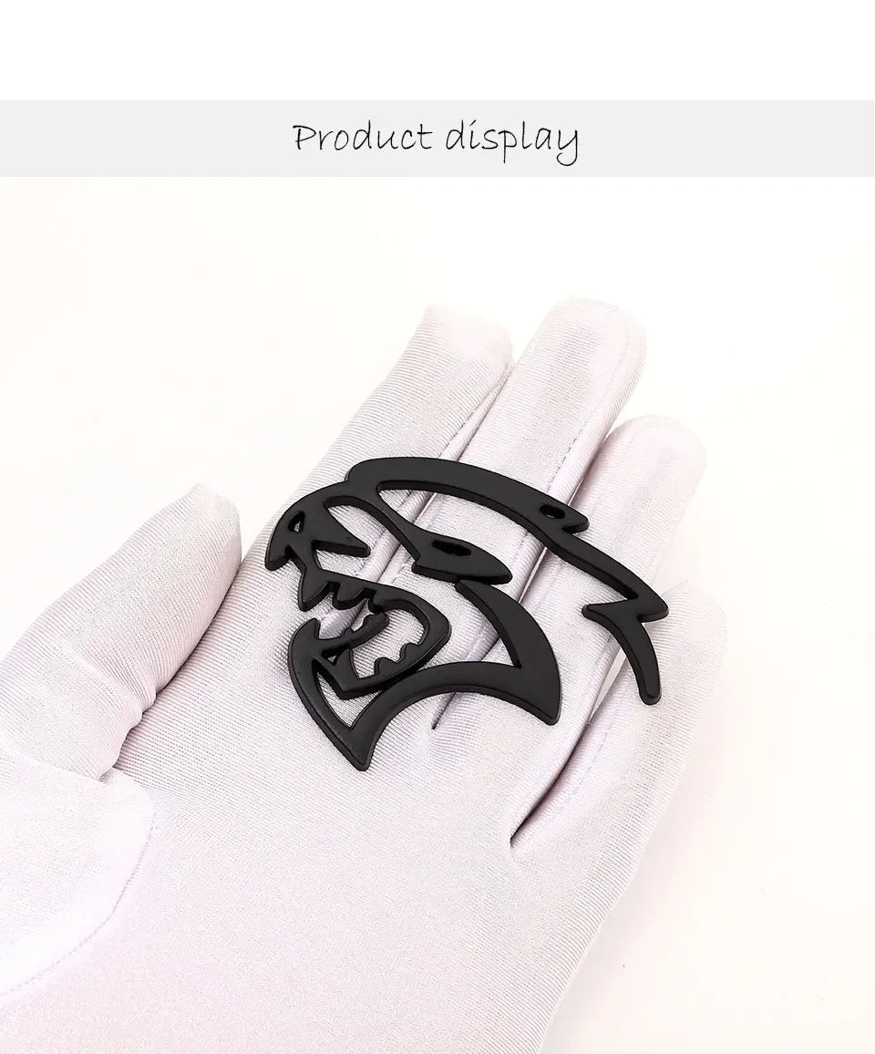 A black custom car body side emblem shaped like a snarling wolf head displayed on a white glove.