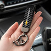 A hand holds a luxury metal keyring set with a black carbon fiber design and a gold Chevrolet emblem.