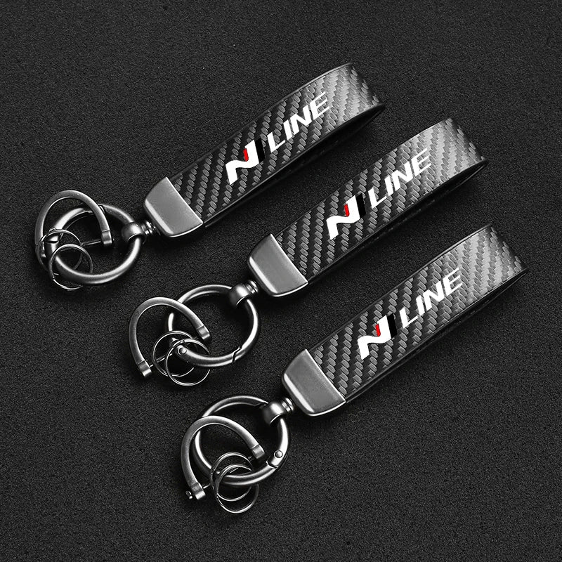 A set of three black carbon fiber style keychains with silver hardware displayed on a dark background.