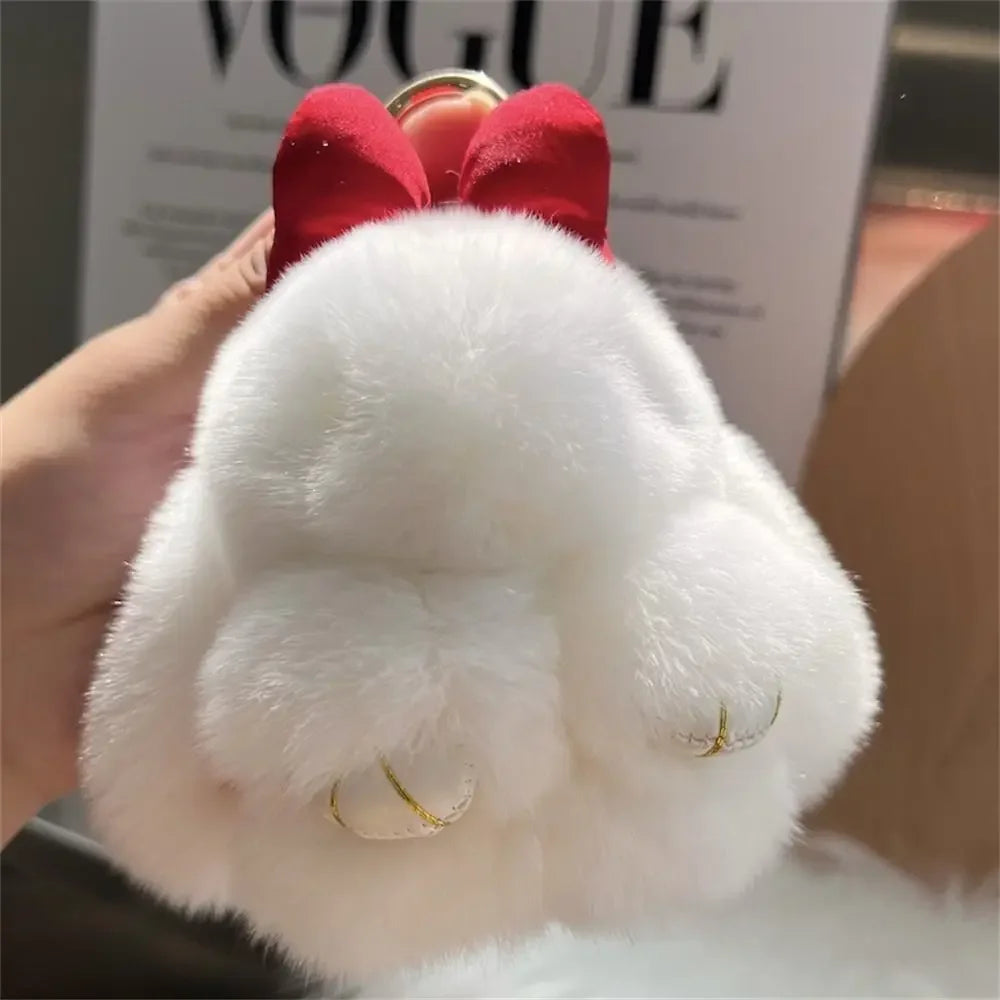A white plush bunny keychain with soft fur and a gold ring is held in a hand.