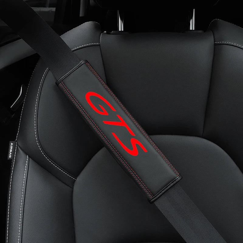 A close-up of a black seat belt protector cover with red GTS lettering on a car seat.