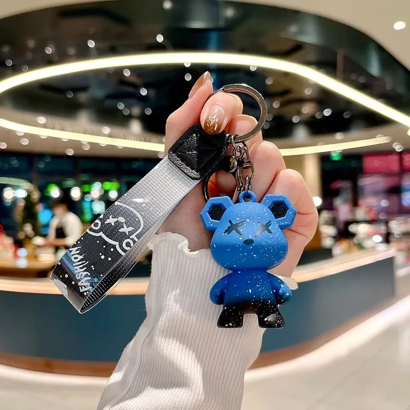 Une main tient une boîte à clés en cuir noir avec un porte-clés argenté, orné d'un charm d'éléphant bleu.